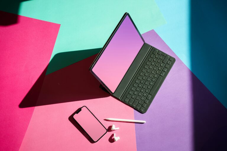 laptop, phone, earbuds and pencil on a colorblock background